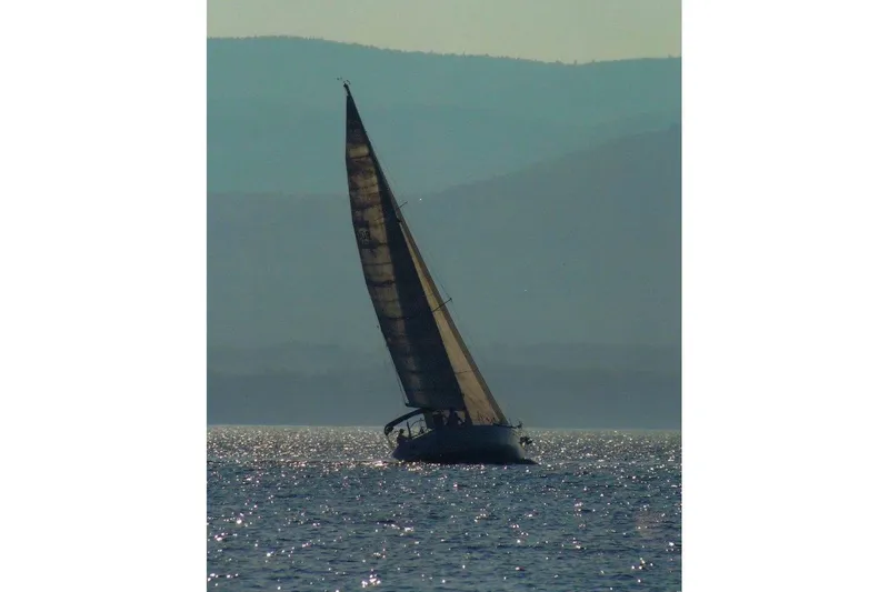 Slide: The Image of Sailboat Beneteau First 38s5 (1991) gliding on shimmering water with mountainous backdrop. - 9