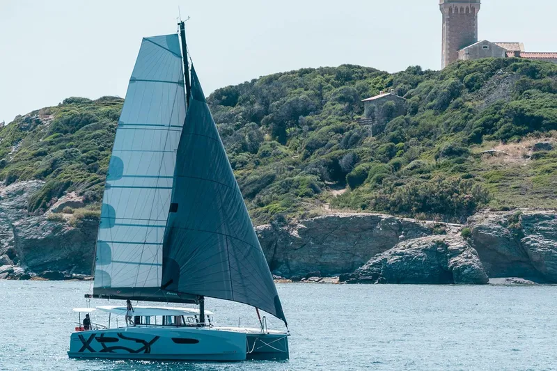 Slide: The Image of Manufacturer Provided Image: Sailing catamaran Excess 13, 2026 model, cruising near rocky coastline with lush greenery. - 8