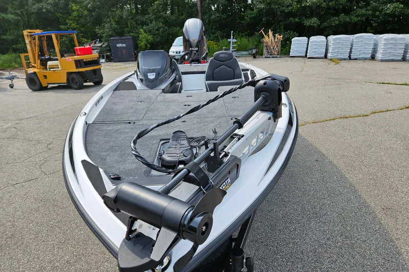 Slide: The Image of 2026 Skeeter ZX150 boat with trolling motor, parked on pavement near forklift and stacked materials. - 8
