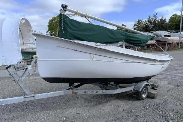 Slide: The Image of 2019 Com-Pac Picnic Cat sailboat on trailer with green cover, parked outdoors. - 2