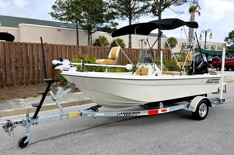 Slide: The Image of 2025 Carolina Skiff 162 JLS boat on trailer, parked outdoors with trees in background. - 19