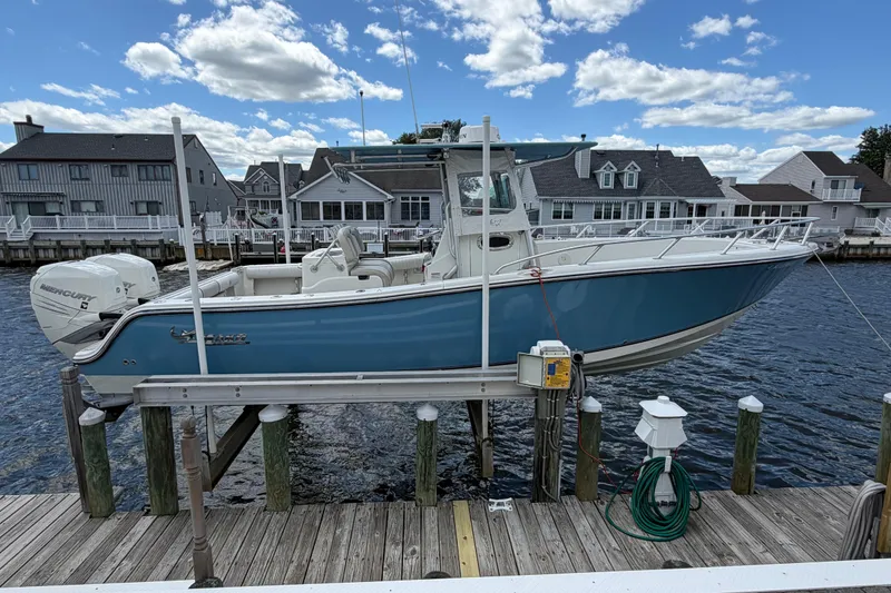 The Image of 2017 Mako 284 Center Console boat docked by waterfront homes under a blue sky. - 1