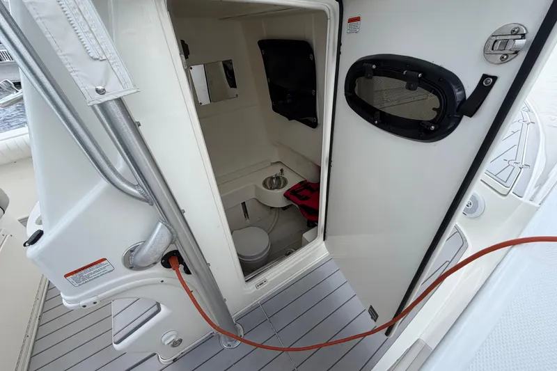 Slide: The Image of 2017 Mako 284 Center Console boat interior with open door, showcasing compact restroom facilities. - 28