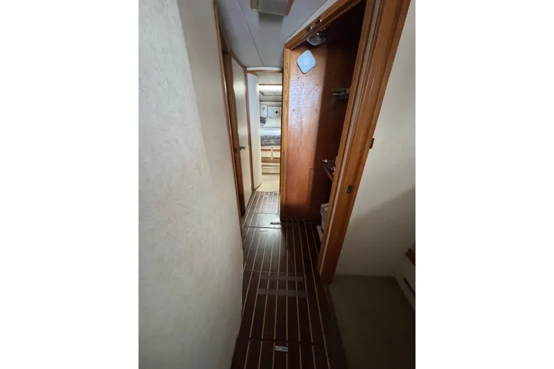 Slide: The Image of Narrow hallway inside 1988 Bertram 50 Convertible yacht with wooden flooring and open door. - 52