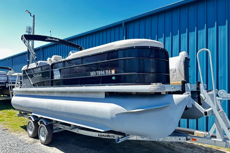 The Image of 2016 Godfrey Sweetwater 2286SB pontoon boat on trailer, parked by blue building. - 0