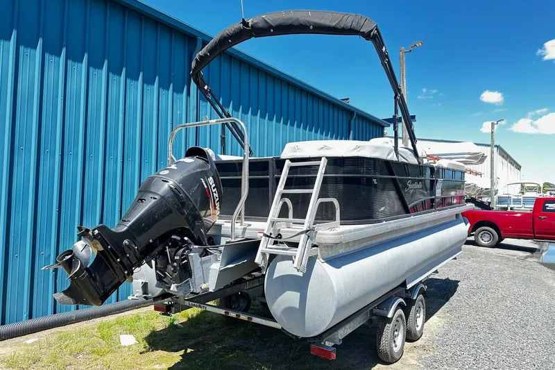 Slide: The Image of 2016 Godfrey Sweetwater 2286SB pontoon boat on trailer, parked near blue building. - 2