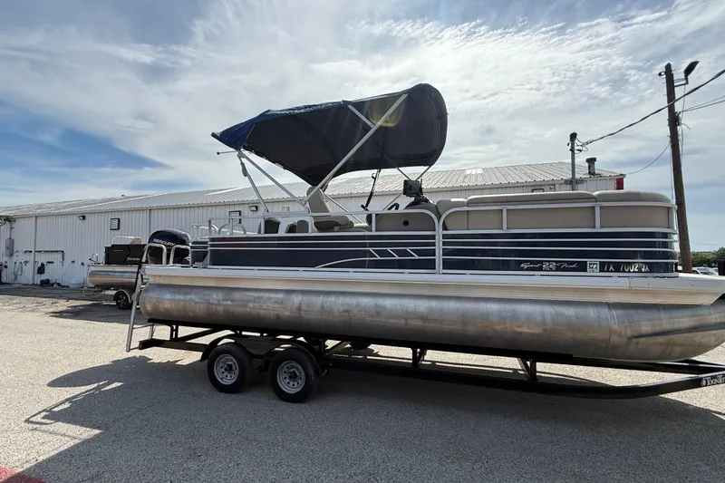 Slide: The Image of 2021 Sun Tracker SportFish 22 DLX pontoon boat with canopy on trailer, parked outdoors. - 3