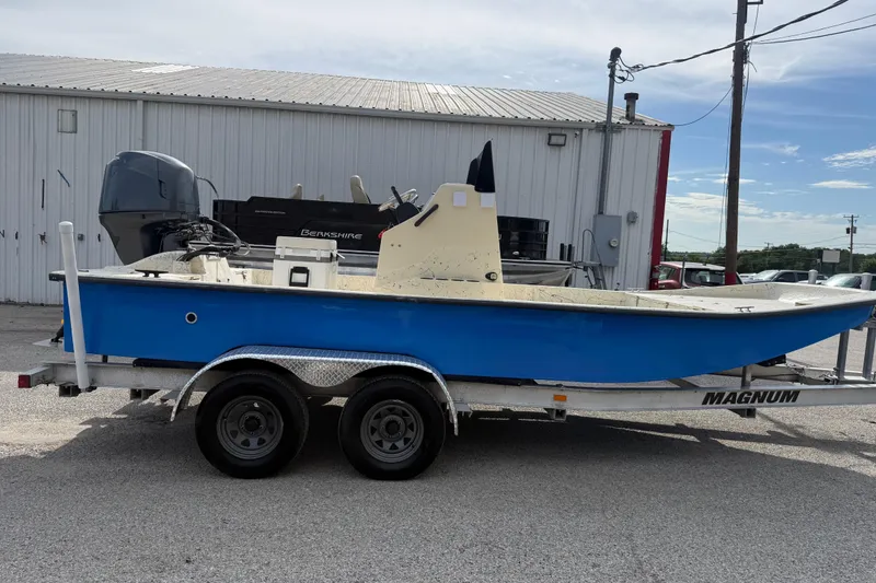 Slide: The Image of 2007 Flats Cat 19 boat on trailer, blue hull, parked outside a warehouse. - 12