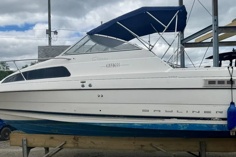 The Image of 2000 Bayliner 2252 Ciera Express boat with blue canopy on a wooden stand. - 0