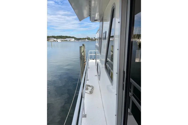 Slide: The Image of 1991 Gibson 37 Standard Houseboat docked, showcasing side deck and serene waterfront view. - 19