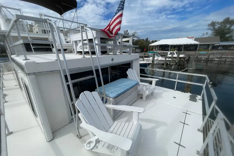 Slide: The Image of 1991 Gibson 37 Standard Houseboat with deck chairs, docked at a marina under a blue sky. - 21
