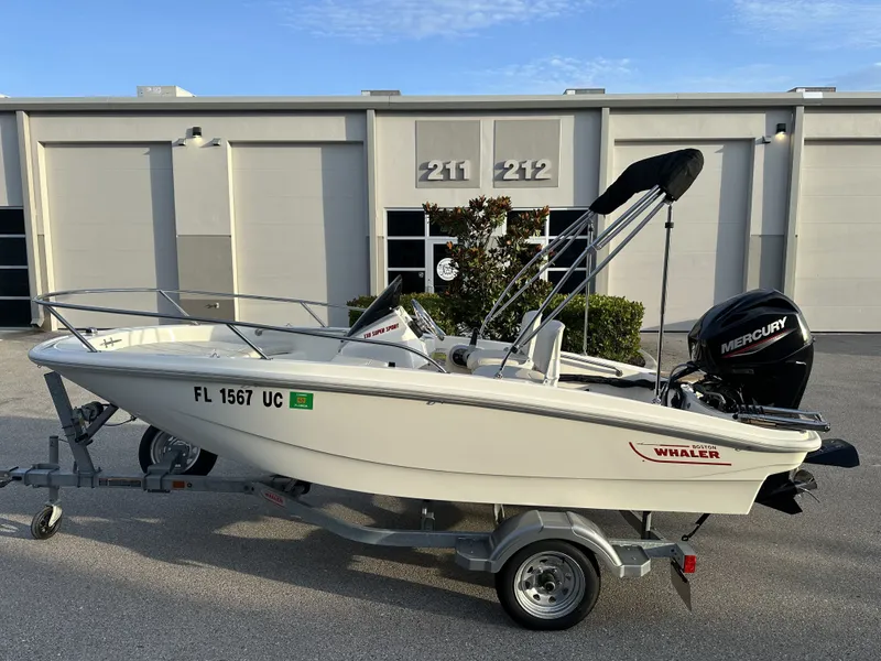 Slide: The Image of 2025 Boston Whaler 130 Super Sport boat on trailer in front of building. - 3