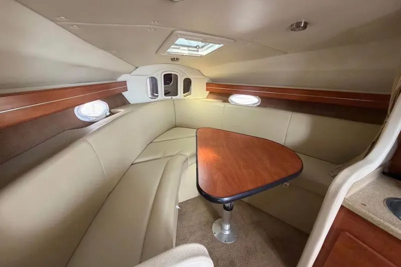 Slide: The Image of 2006 Rinker 300 Express Cruiser cabin with beige seating and wooden table. - 10