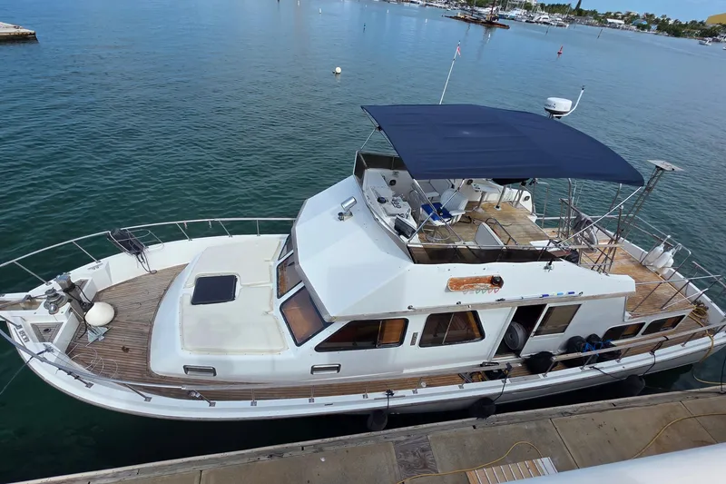 Slide: The Image of 1991 Marine Trader Trawler docked, featuring spacious deck and canopy, in serene marina setting. - 1