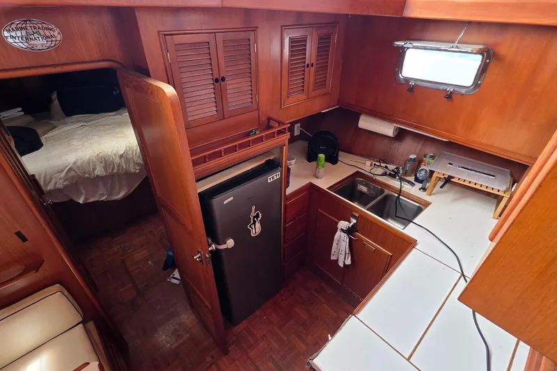 Slide: The Image of 1991 Marine Trader Trawler kitchen with wooden cabinetry, compact fridge, and sink area. - 4