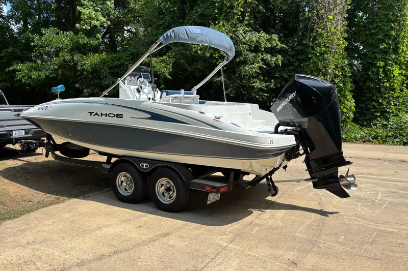 Slide: The Image of 2020 Tahoe 2150 CC boat on trailer, parked outdoors with lush greenery background. - 2