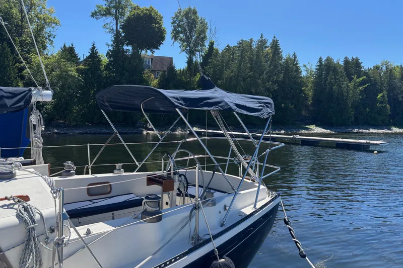 Slide: The Image of 1979 Aloha 34 sailboat docked by a serene, tree-lined shoreline. - 42