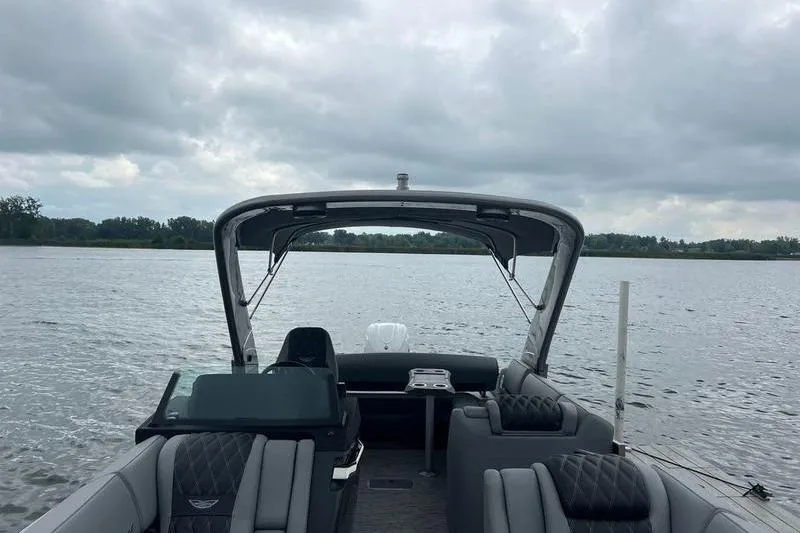 Slide: The Image of 2026 Bennington RX 25 RXSBA pontoon boat on a lake under cloudy skies. - 2