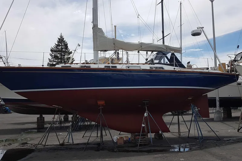 Slide: The Image of 1984 Ohlson 38 sailboat on stands, blue hull, red keel, in a boatyard. - 56
