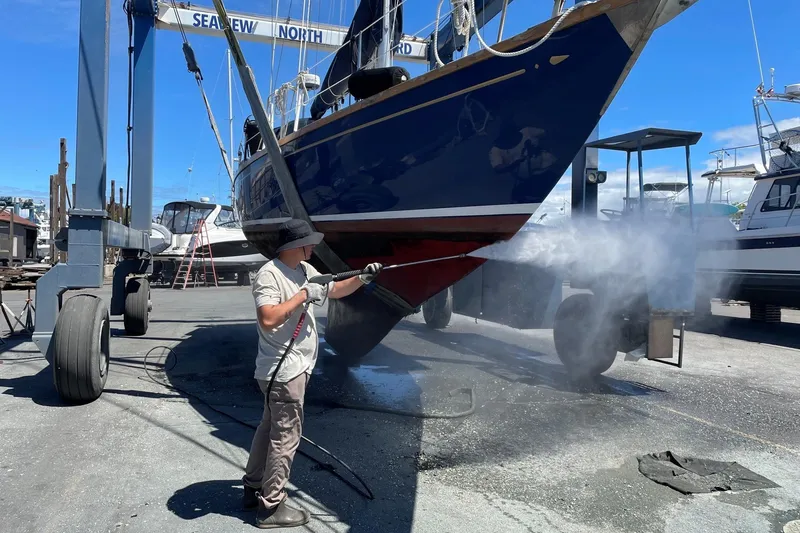 Slide: The Image of Person pressure washing a 1984 Ohlson 38 sailboat hull at a boatyard. - 57