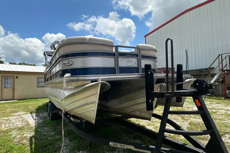 Slide: The Image of 2017 Manitou 25 SES pontoon boat on trailer, parked outdoors under a cloudy sky. - 1
