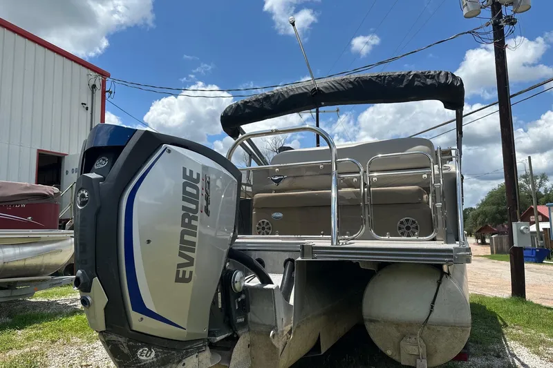Slide: The Image of 2017 Manitou 25 SES pontoon boat with Evinrude engine, parked outdoors under blue sky. - 2