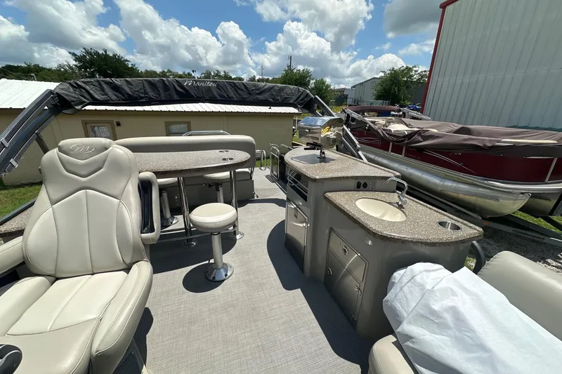 Slide: The Image of 2017 Manitou 25 SES boat interior with seating, table, and kitchenette under a sunny sky. - 5