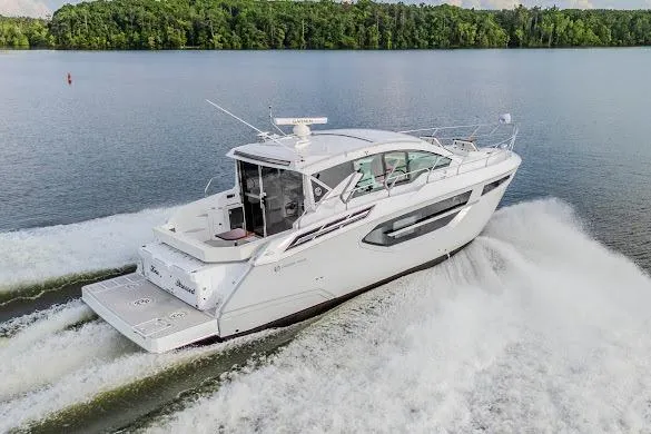 The Image of 2023 Cruisers Yachts 42 Cantius cruising on a serene lake with lush green shoreline. - 0