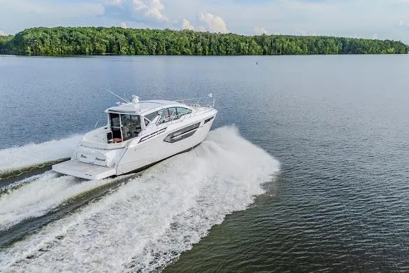 Slide: The Image of 2023 Cruisers Yachts 42 Cantius cruising on a serene lake with lush green shoreline. - 26