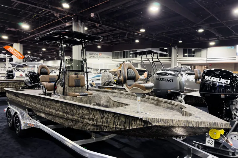 Slide: The Image of 2026 Excel 220 Bay Pro Elite boat displayed at an indoor boat show with Suzuki engines. - 2