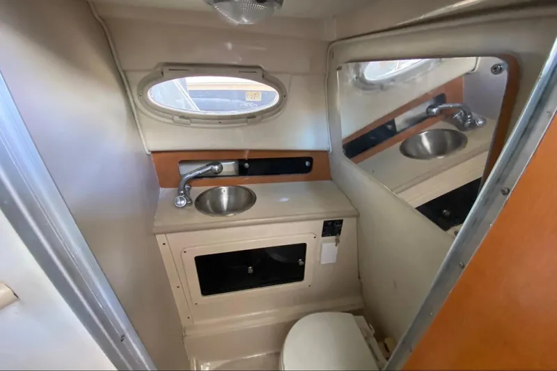 Slide: The Image of 2017 Robalo R265 Walkaround boat bathroom with sink, mirror, and porthole window. - 7