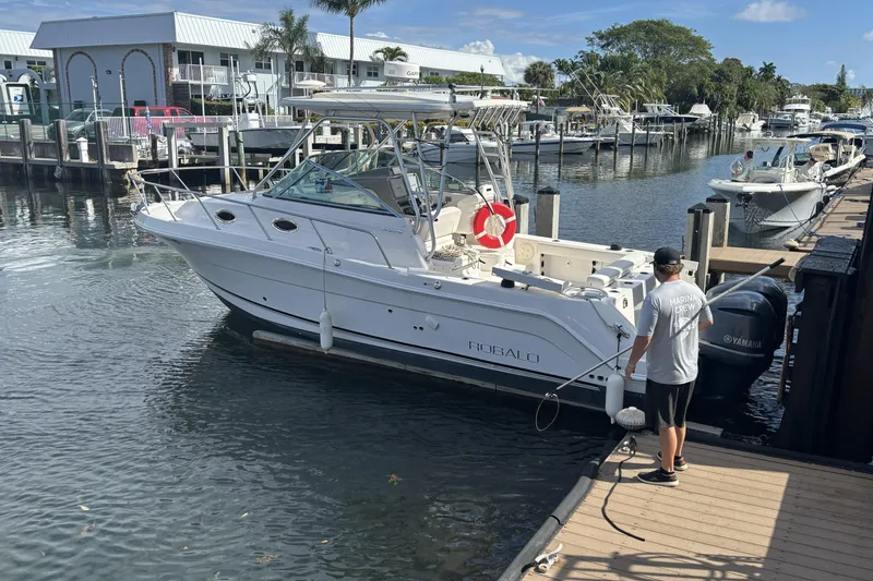 Slide: The Image of 2014 Robalo R305 Walkaround boat docked at marina with crew member. - 10