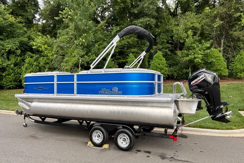 Slide: The Image of 2026 Sun Tracker Party Barge 20 DLX pontoon boat on trailer, parked near lush greenery. - 3