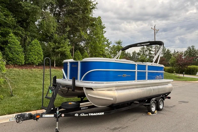 Slide: The Image of 2026 Sun Tracker Party Barge 20 DLX pontoon boat on trailer, parked outdoors. - 2