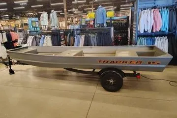 The Image of 2026 Tracker Grizzly 15 Jon boat displayed indoors, surrounded by clothing racks. - 0