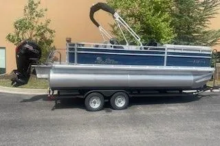 The Image of 2026 Sun Tracker SportFish 20 DLX pontoon boat on trailer, parked outdoors. - 0
