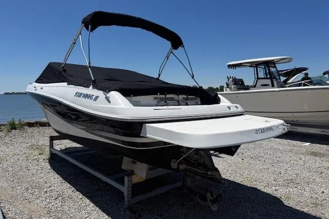 Slide: The Image of 2002 Four Winns 220 Horizon boat with black canopy on gravel near water. - 2