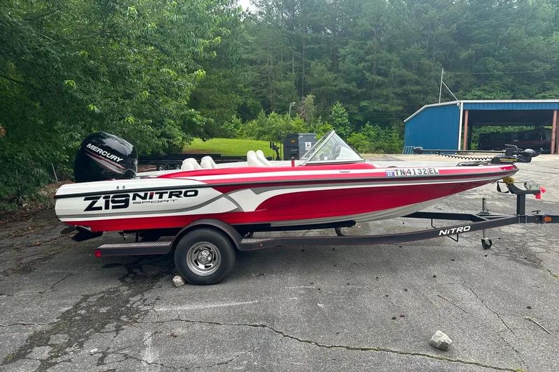 Slide: The Image of 2017 Nitro Z19 Sport boat on trailer, parked outdoors near trees and a blue building. - 11