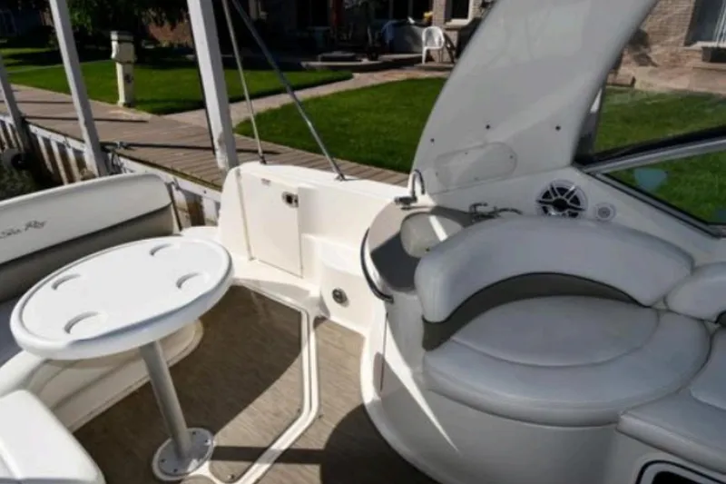 Slide: The Image of 2006 Sea Ray Sundancer 260 boat interior with seating and table, docked by a lawn. - 2