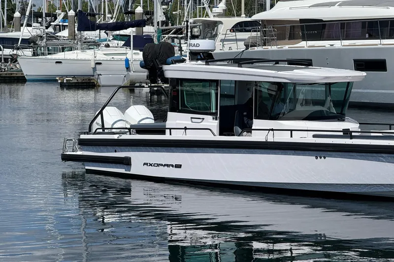 Slide: The Image of 2022 Axopar Brabus 28 Cabin boat docked in a marina, surrounded by yachts. - 1
