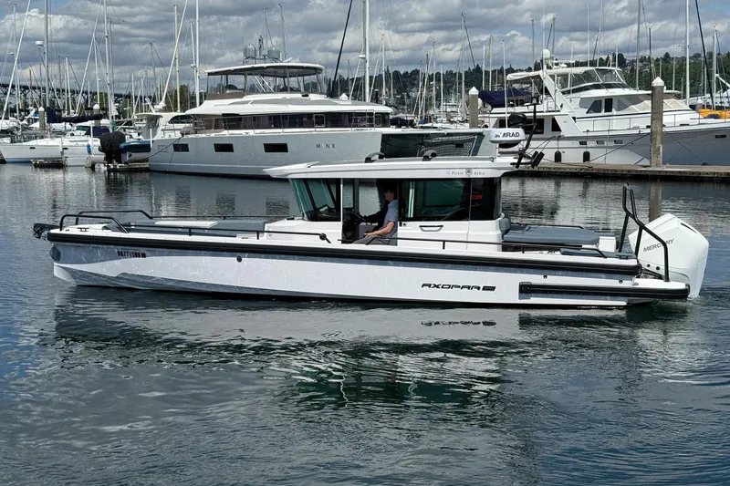 Slide: The Image of 2022 Axopar Brabus 28 Cabin boat docked in a marina with yachts in the background. - 16