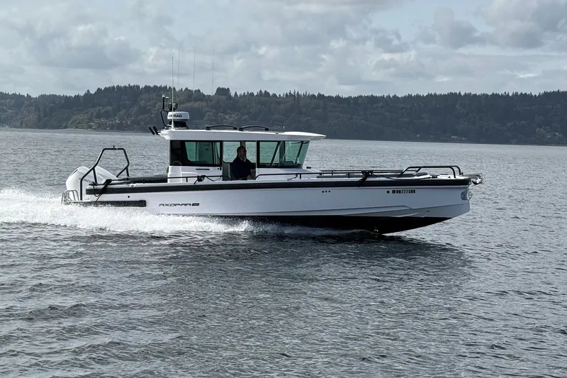 The Image of 2022 Axopar Brabus 28 Cabin cruising on a scenic lake with forested shoreline. - 0
