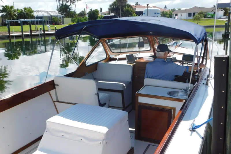 Slide: The Image of 1995 Lyman 27 Cruisette boat with canopy, docked in a serene waterfront setting. - 11