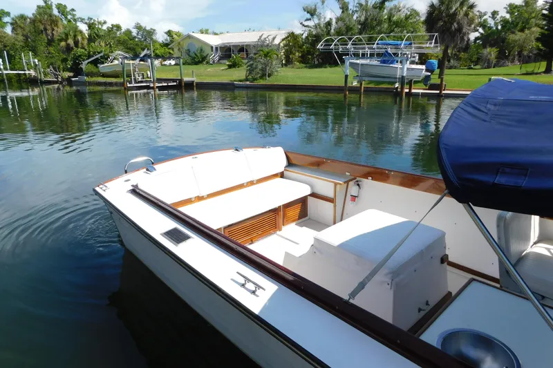 Slide: The Image of 1995 Lyman 27 Cruisette boat docked on a serene waterfront with lush greenery. - 19