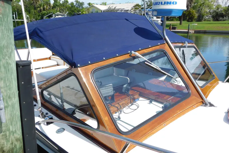 Slide: The Image of 1995 Lyman 27 Cruisette boat with blue canopy docked by a serene waterfront. - 8