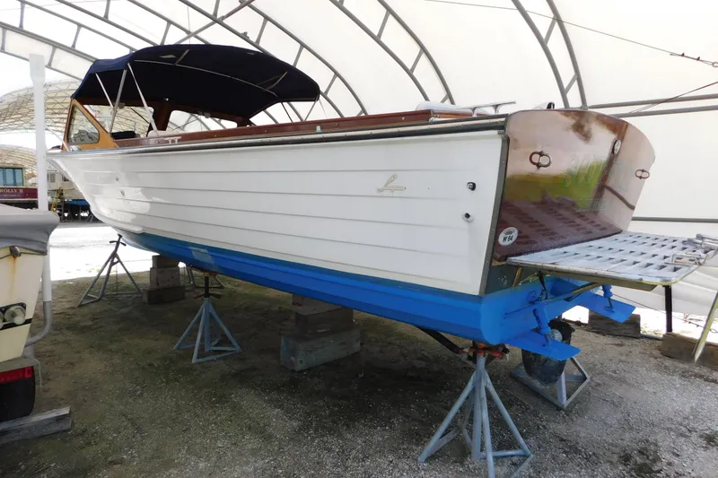 Slide: The Image of 1995 Lyman 27 Cruisette boat on stands, under a canopy, with blue hull and white deck. - 35