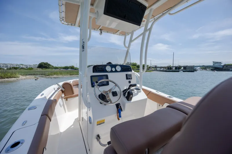 Slide: The Image of 2022 Pioneer 202 Islander boat interior with steering wheel, dashboard, and seating on a sunny day. - 16