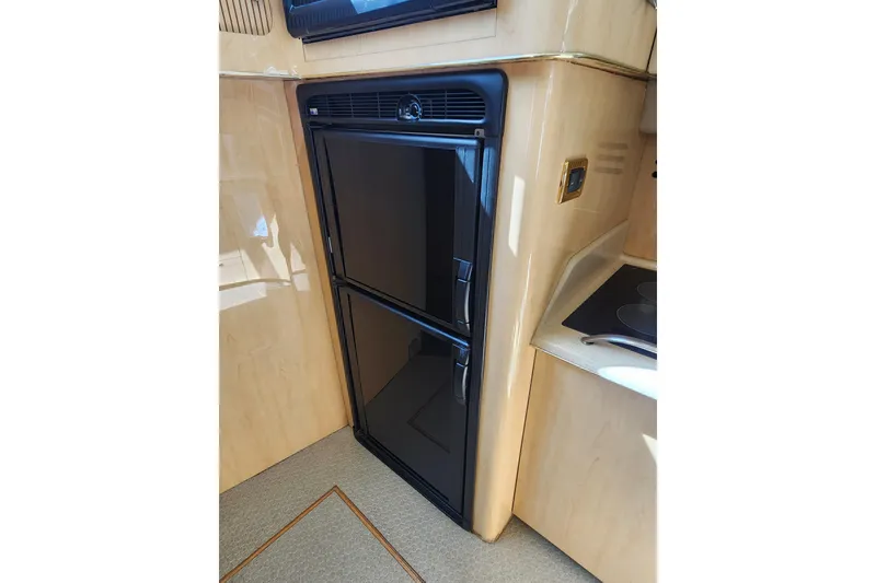 Slide: The Image of 2001 Sea Ray 400 Sedan Bridge yacht kitchen with black refrigerator and beige cabinetry. - 16