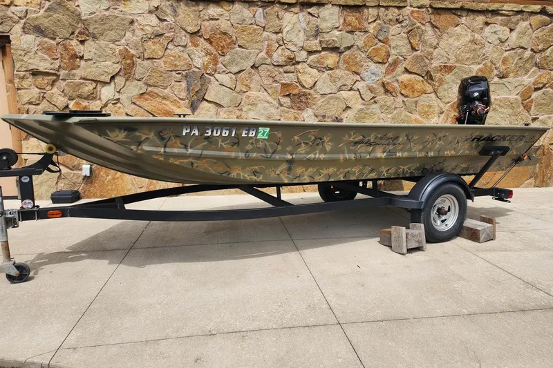 The Image of 2022 GRIZZLEY 1654SPT boat on trailer, camouflage design, parked on concrete. - 0