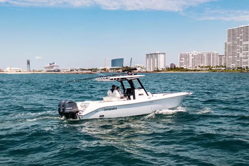 Slide: The Image of 2021 Everglades 295 Center Console boat cruising near city skyline on a sunny day. - 2